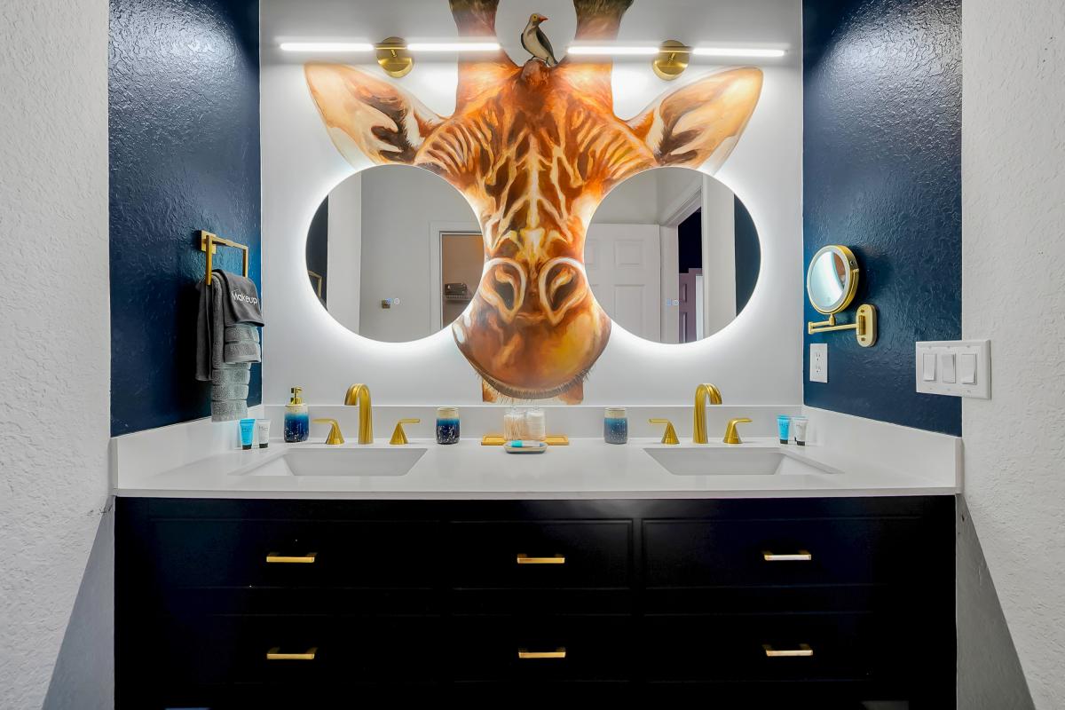 Spa-inspired en-suite with double vanity, bold mural, backlit mirrors, and luxe gold finishes.